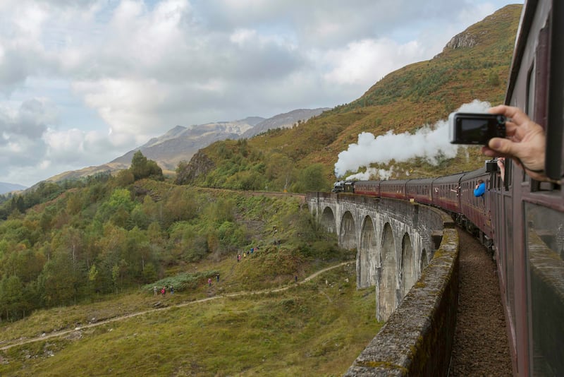 Passengers filming on their phones and cameras out of the window of the Jacobite Steam Train as it makes its way along the Glenfinnan Viaduct
