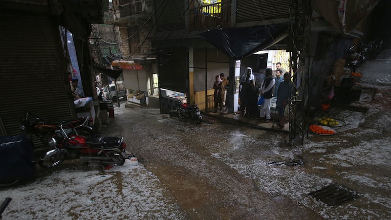 People stand inside a shop due to heavy hailstones rain in Peshawar