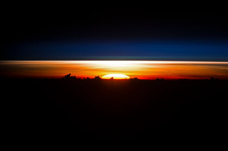 partial disc of the sun just as it began to rise, creating a sheet of light across the horizon. Silhouetted clouds give the sense of a jumbled mountain range. (Nasa)