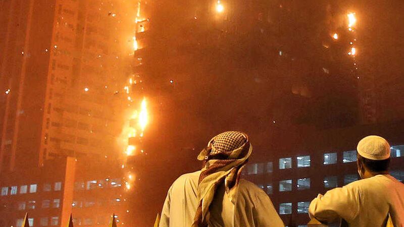 Two Emirati officials watch as a fire spreads up the side of a high-rise building in Ajman, United Arab Emirates. Picture by Kamran Jebreili, Associated Press