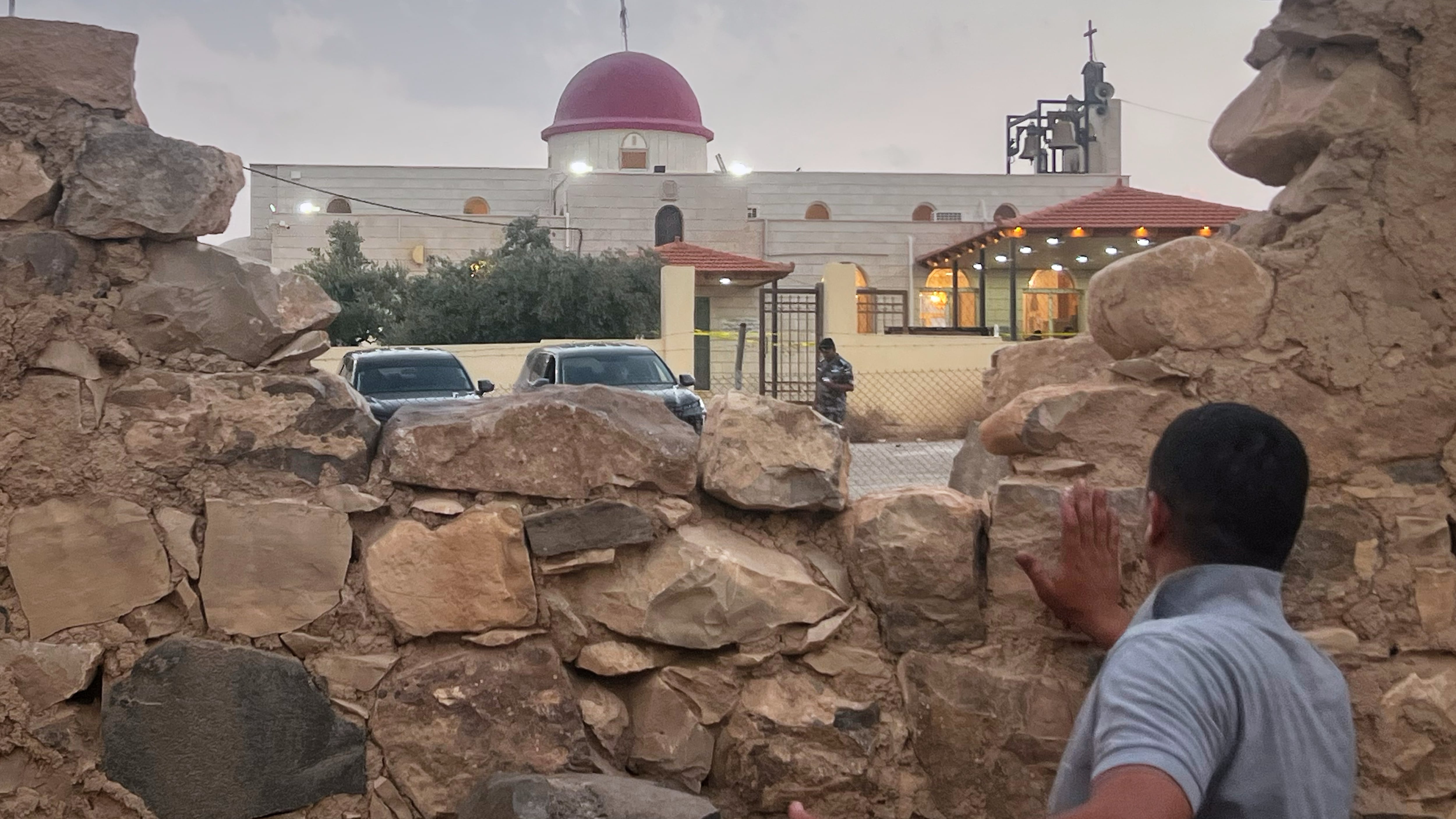 A man looks through a gap in a stone wall toward a Greek Orthodox church where gunmen opened fire during a funeral hours earlier in Hamoud village, in Jordan’s Karak governorate (AP)