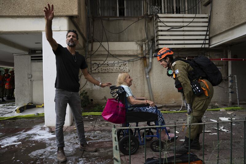 An Israeli man evacuates an elderly woman from a building struck by a rocket fired from Gaza, in Tel Aviv (AP)