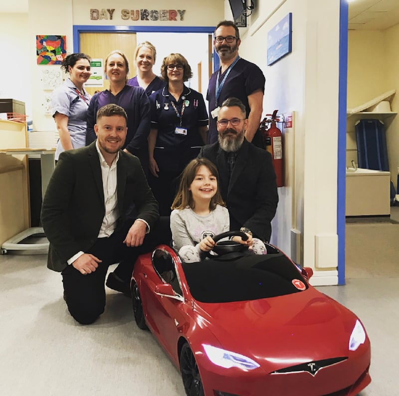 Juno in the driving seat of the Tesla, surrounded by staff