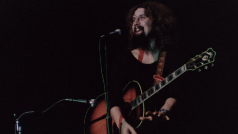 A photo of Billy Connolly on stage with his guitar during his Irish tour of 1975, as captured in the film Big Banana Feet