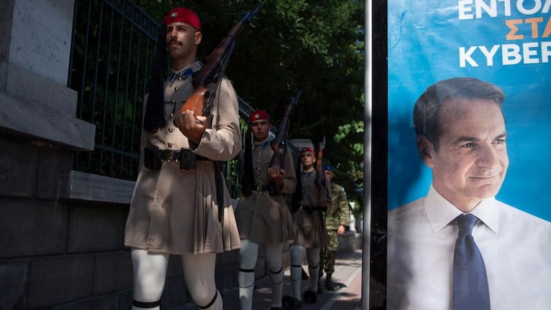 Soldiers of the Presidential Guard, known as Evzones, pass next to an election banner of the Nea Dimokratia political party, in Athens (Michael Varaklas/AP)