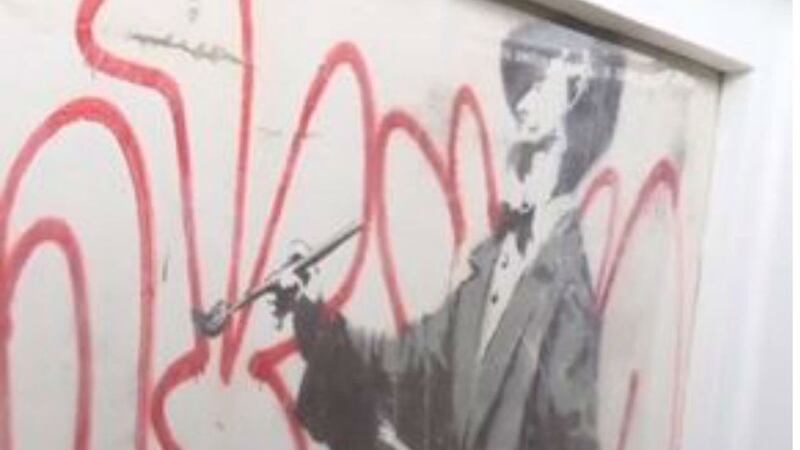The mural depicts an artist writing ‘Banksy’ in bold red letters.