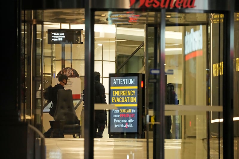 Police officers walk past a sign to evacuate at the shopping centre (Rick Rycroft/AP)