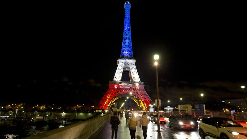 People walk towards the illuminated Eiffel Tower in the French national colors red, white and blue in honor of the victims of the attacks in Paris. Picture by Peter Dejong, AP&nbsp;