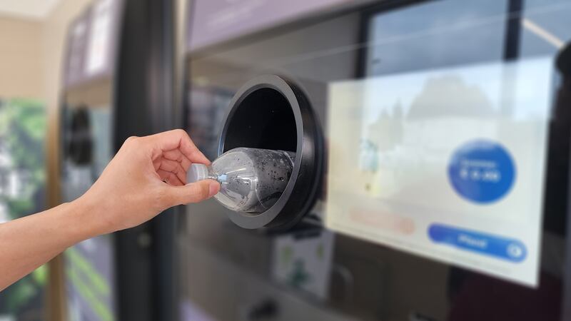 Hand inserts plastic bottle into automated recycling machine.