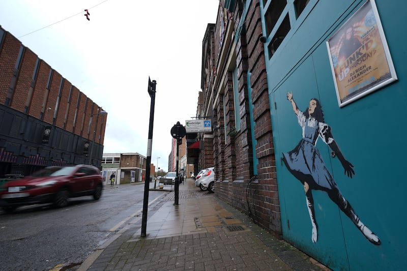 The mural depicts Dorothy from The Wizard Of Oz reaching skywards, towards a pair of ruby slippers which are hanging from a nearby cable