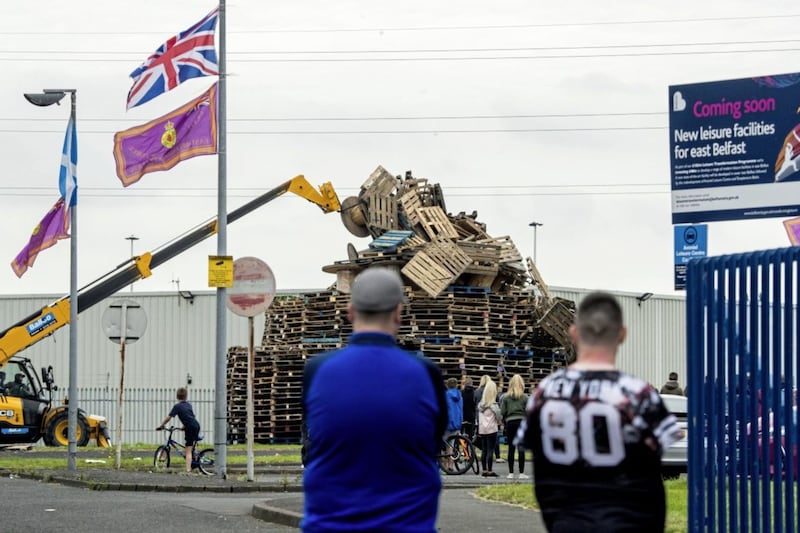 A crowd gathers to watch men remove material from a July 11th night bonfire at Avoniel Leisure Centre shortly after a Belfast City Council committee voted to send contractors in to remove material. Picture by PA Wire