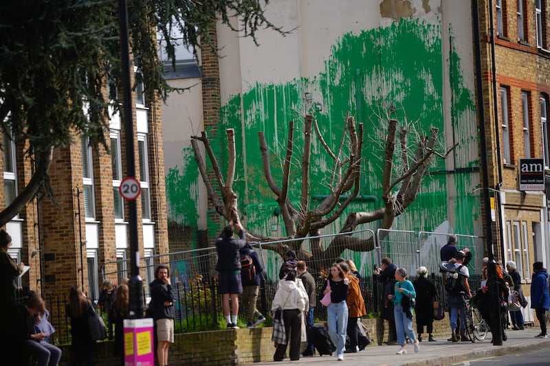 People gather to look at the Banksy artwork on the side of a building in Finsbury Park, London, in March