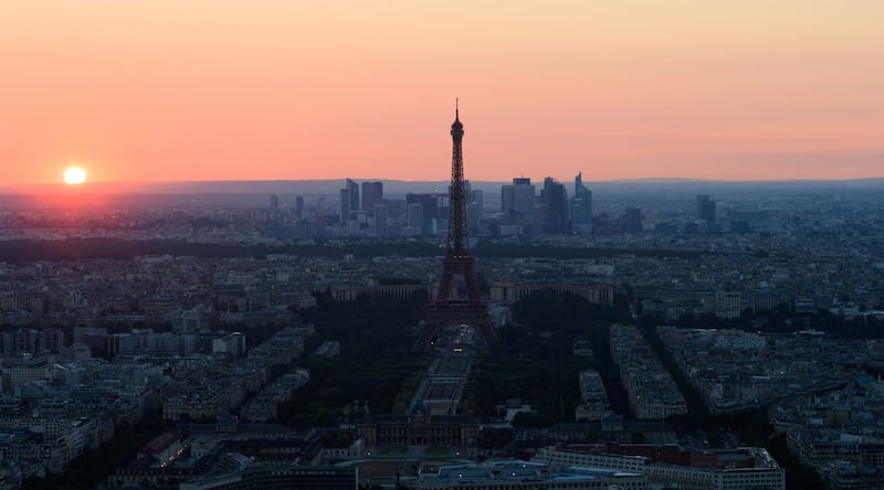 The sun sets behind the Eiffel Tower and the skyscrapers of La Defense (John Walton/PA)