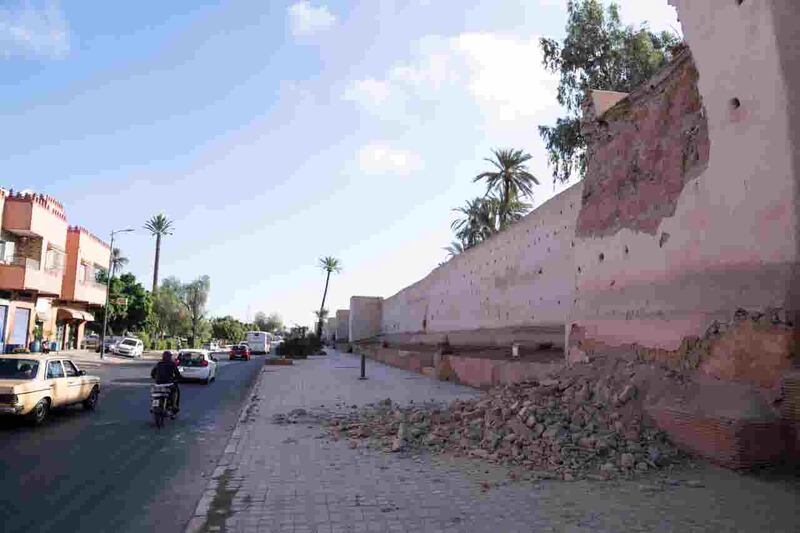People drive past a damaged wall of the historic Medina of Marrakesh