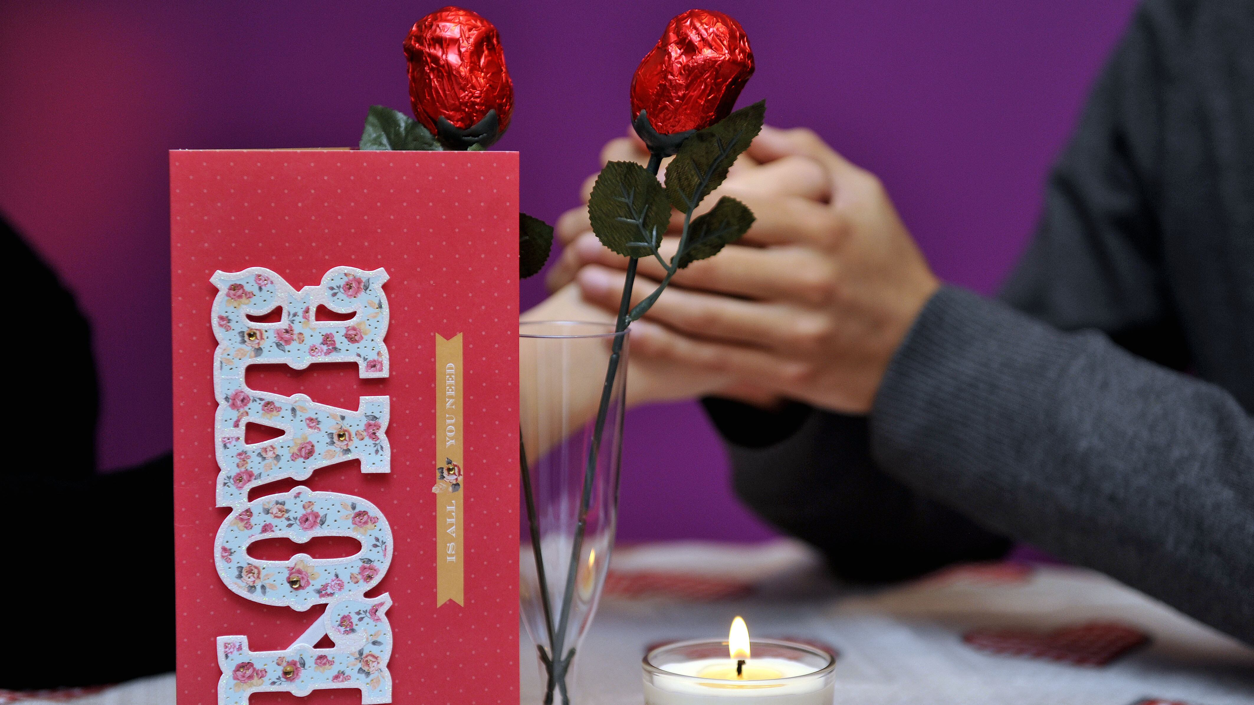 Picture posed by models of a couple with valentines gifts of a card, chocolates and chocolate roses in a glass