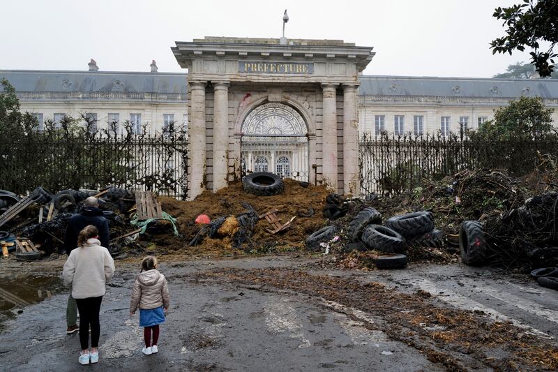 People watch slurry, manure and tyres dumped by farmers at the entrance of the local state administration building, in Agen (AP Photo/Fred Scheiber)
