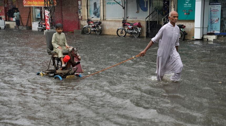 A man pulls a handcart carrying a boy as they wade through a flooded road in Lahore (KM Chaudary/AP)