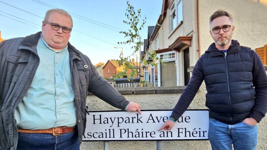 SDLP councillors Séamus de Faoite and Gary McKeown pictured at one of the signs that will be replaced. Picture from Séamus de Faoite/Twitter