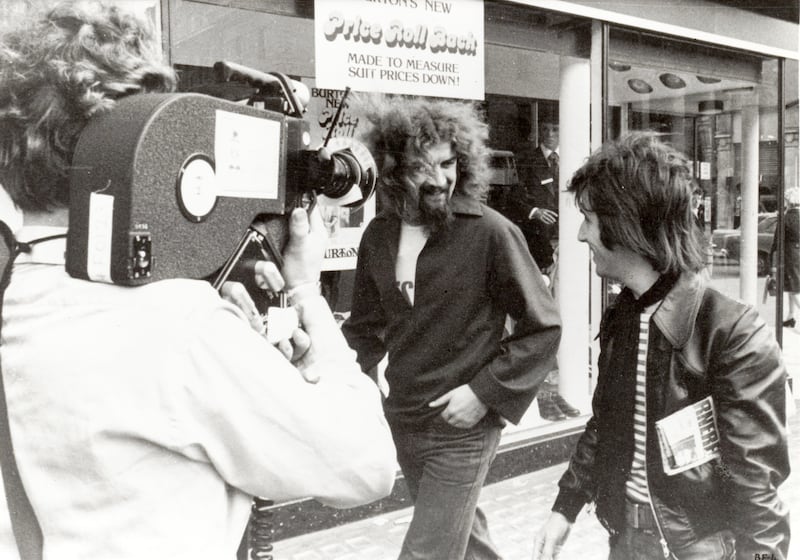 A back and white image of director Murray Grigor and cinematographer David Peat with Billy Connolly on the streets of Ireland circa 1975 from the film Big Banana Feet