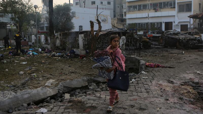A Palestinian girl carries a blanket as she walks past the site of a deadly explosion at al Ahli hospital, in Gaza City (Abed Khaled/AP/PA)