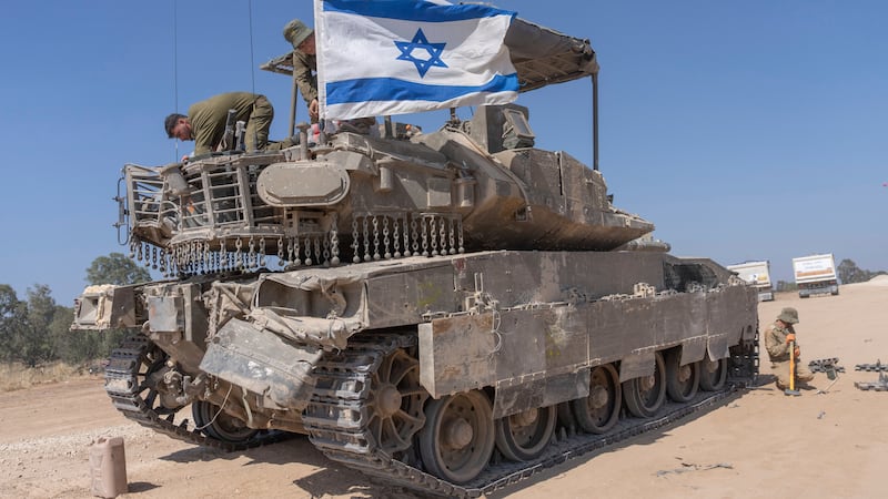 An Israeli soldier attaches an Israeli flag on top of an armoured personnel carrier in southern Israel (Ohad Zwigenberg/AP)