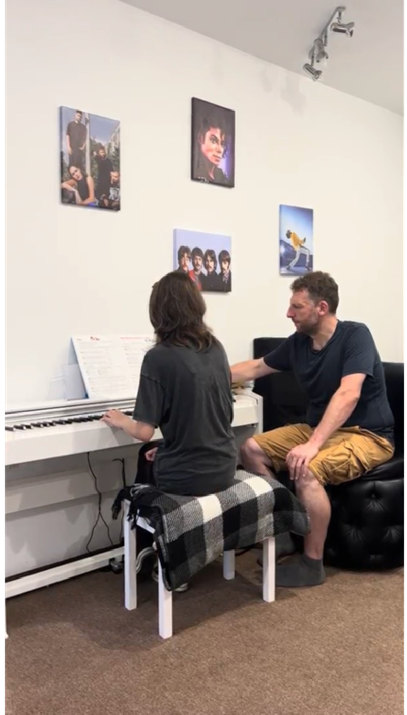 Man sitting next to girl playing the piano