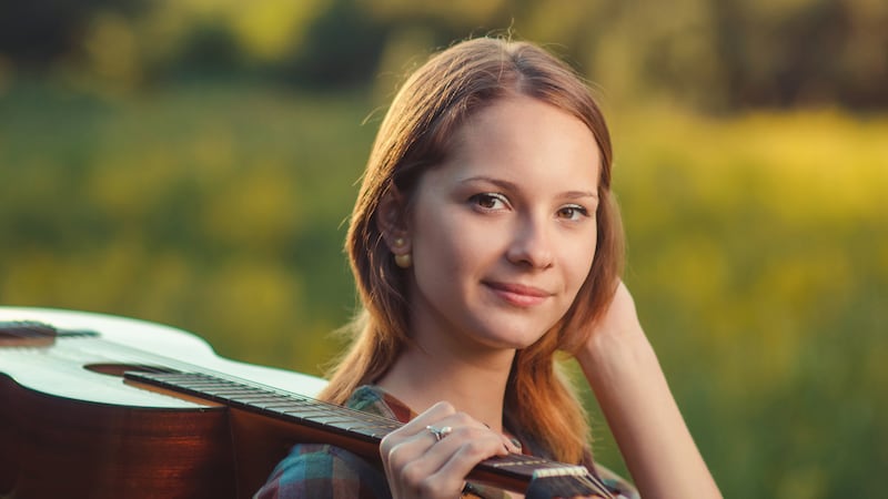 Portrait of a musician young woman in plaid shirt with a acoustic wooden guitar on shoulder on colorfull summer background.