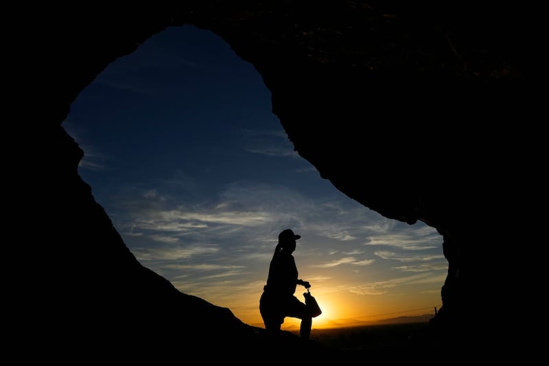 A hiker walks past the Hole-in-the-Rock at Papago Park during sunrise in Phoenix