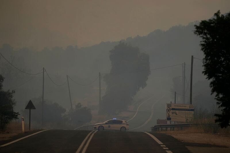 A police car blocks a road as the smoke from the wildfire engulfs the village of Agia Sotira, near Athens