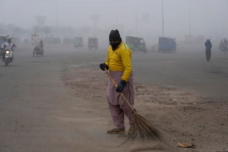 A sweeper wears a scarf over his face as smog envelops Lahore (KM Chaudary/AP)