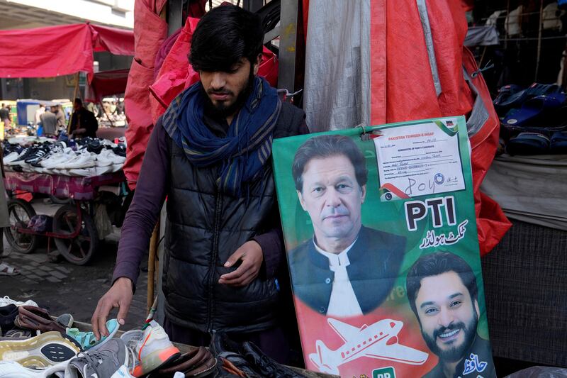 A vendor arranges shoes next to an election campaign poster of Pakistan’s jailed Former Prime Imran Khan party’s candidate for parliamentary election at a market, in Lahore, Pakistan (KM Chaudary/AP)