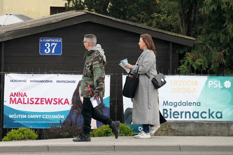 Campaigners with flyers walk past electoral posters of candidates in the local elections in Kazun Polski, near Warsaw (Czarek Sokolowski/AP)