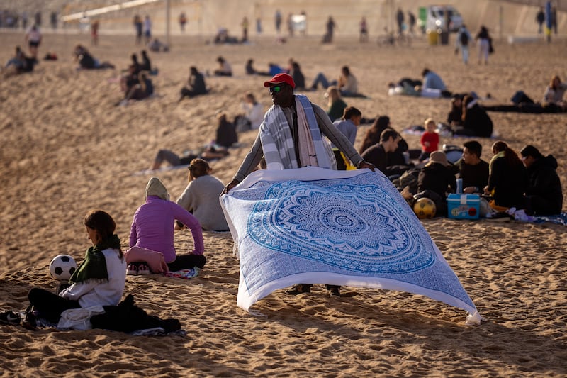 A street vendor displays sheets for sale while people sunbathe on the beach in Barcelona, Spain on January 26 (AP)