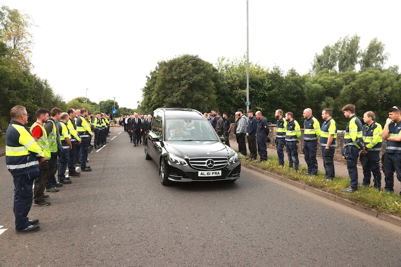 Employees stand outside the Wrightbus factory in Ballymena, as they watch the passing cortege