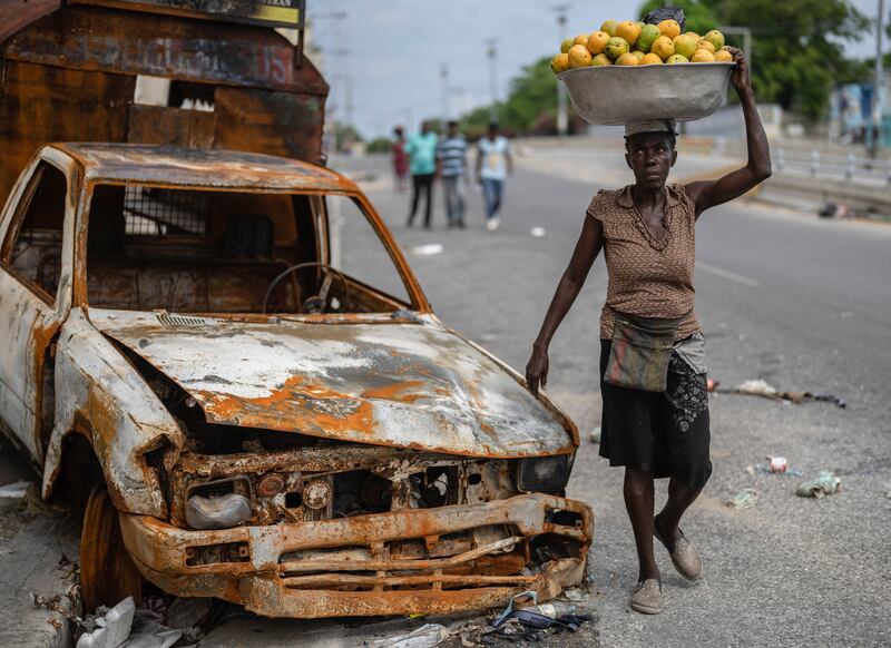 A fruit vendor walks by a burned car in the Delmas district of Port-au-Prince (AP Photo/Ramon Espinosa)