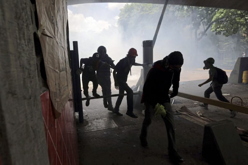 Students run from tear gas fired by National Police outside the Central University of Venezuela in Caracas, Thursday, May 4, 2017. Students held demonstrations across Caracas Thursday as a two-month-old protest movement that shows no signs of letting up claimed more lives. (AP Photo/Fernando Llano). 