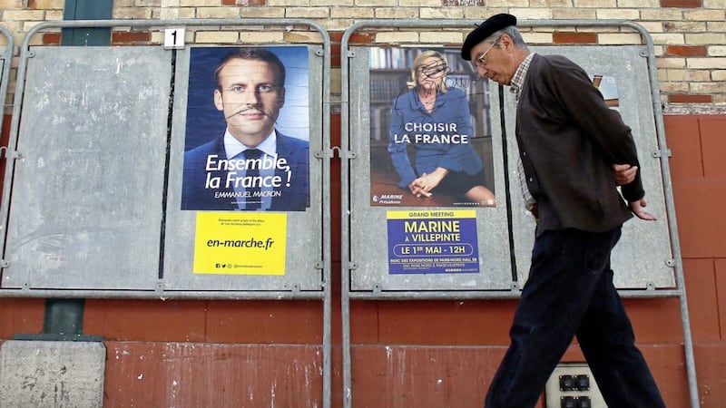 A man walks past defaced election campaign posters for French centrist presidential candidate Emmanuel Macron and far-right candidate Marine Le Pen, in Saint Jean de Luz, southwestern France Picture by Bob Edme/AP 