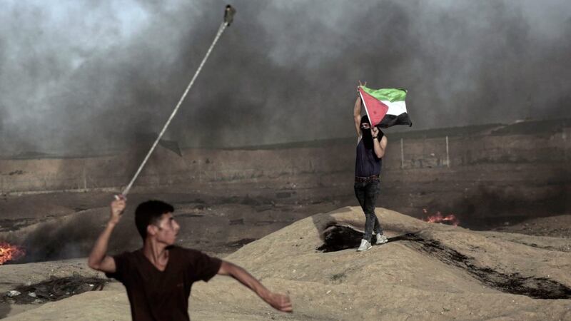 A protester hurls stones at Israeli troops as another holds a Palestinian flag during a protest at the Gaza Strip&#39;s border with Israel last week. Picture by AP Photo/Khalil Hamra 