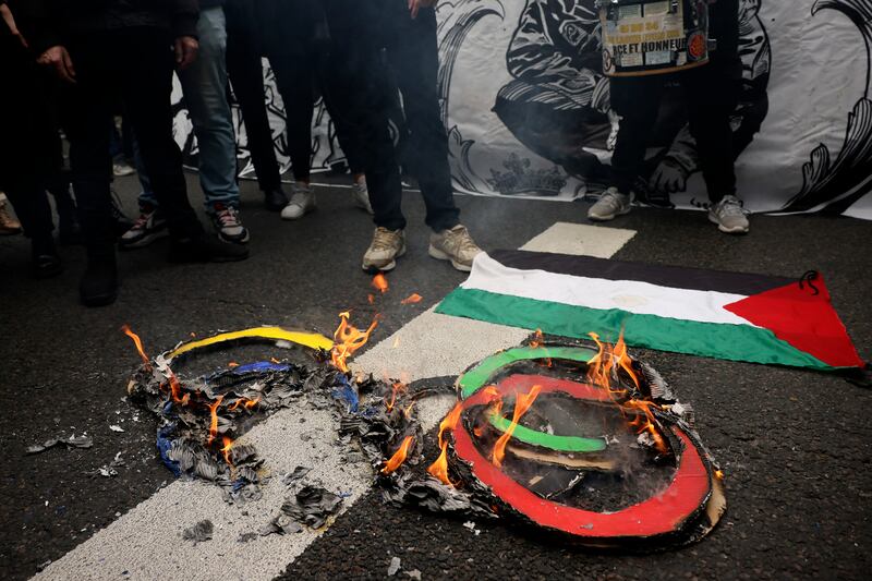 Protesters burn Olympic rings on the pavement near a Palestinian flag during the May Day demonstration in Paris (Thomas Padilla/AP)