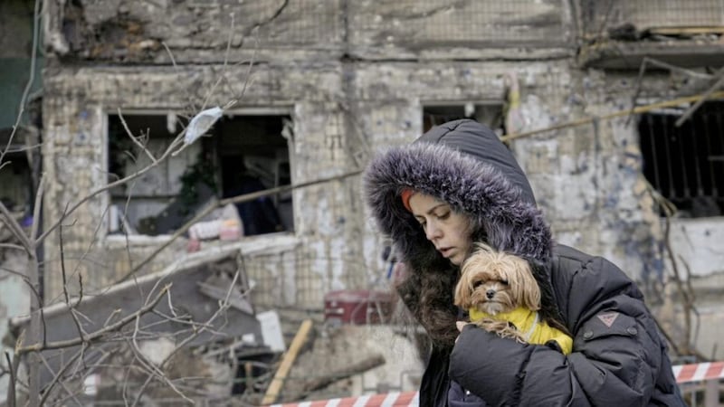 A woman holding a small dog walks in front of an apartment in a block which was destroyed by an artillery strike in Kyiv, Ukraine, yesterday. Picture by Vadim Ghirda, Associated Press 