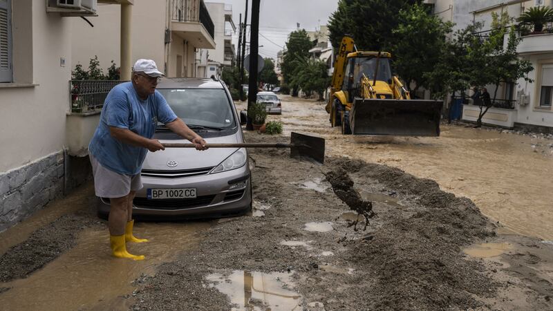 A man shovels mud outside his house in a flooded street in Volos (Petros Giannakouris/AP)