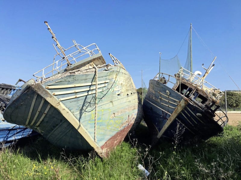 Two old fishing boats used to bring refugees from Libya to Lampedusa lie rotting in the boat yard. 