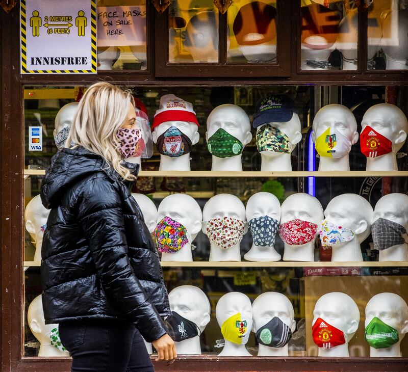 &nbsp;Ciara McCartney walks past a face covering display at Innisfree Newsagents in Belfast.