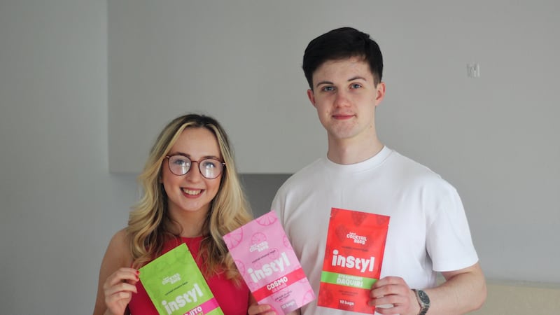 Co-founders of Instyl Brogán Brady and Conleth Mallon holding their products. Photo of the products - a green packet saying 'Instyl Mojito lime mint,' a pink packet saying 'Instyl Cosmo orange,' and a red packet saying 'Strawberry Daquiri.'