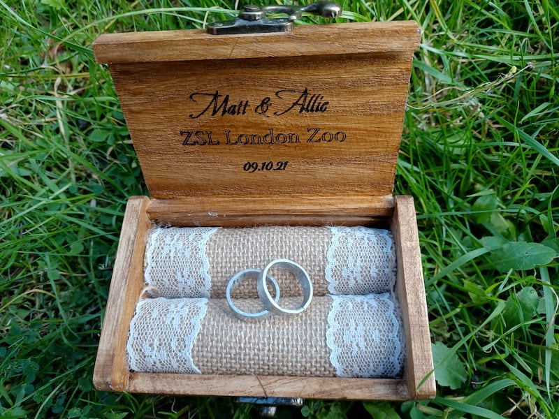 Two silver rings sit within a light brown wooden box on a green background