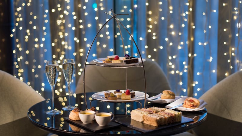 Image of an afternoon tea. There's two glasses of prosecco, a cake stand with a selection of bakes on it and finger sandwiches.