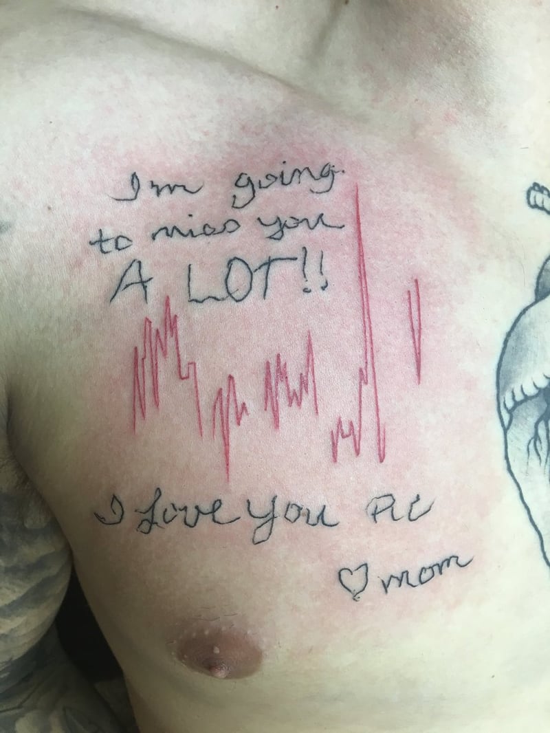A red and raw tattoo of a heartbeat as seen on a heartbeat monitor on a man's chest, with a note in rough handwriting above and below.