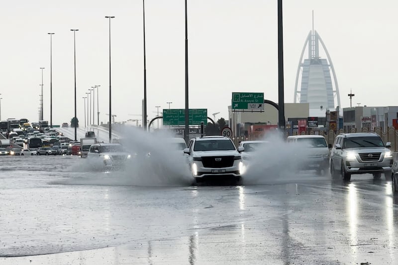 An SUV splashes through standing water on a road in Dubai, with the Burj Al Arab luxury hotel seen in the background (Jon Gambrell/AP)