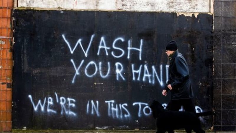 &nbsp;A man walking a dog strolls past graffiti on the Lower Newtownards Road in Belfast with the writing, &Ograve;Wash Your Hands, We&Otilde;re In This Together&Oacute;.