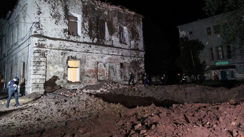 Police offices walk in front of a crater after a Russian rocket attack on a psychiatric hospital in Kharkiv, Ukraine on Saturday (Yakiv Liashenko/AP)